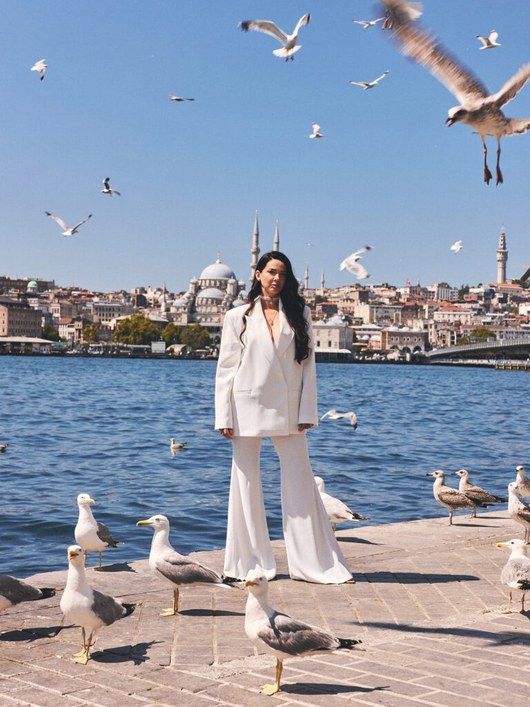 Jelena wearing a Laleon choker in a white suit, standing by the Bosphorus with the Istanbul skyline and seagulls in flight