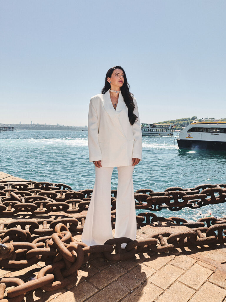 Jelena wearing a Laleon choker and pendant necklace in a white suit, standing by the Bosphorus in Istanbul
