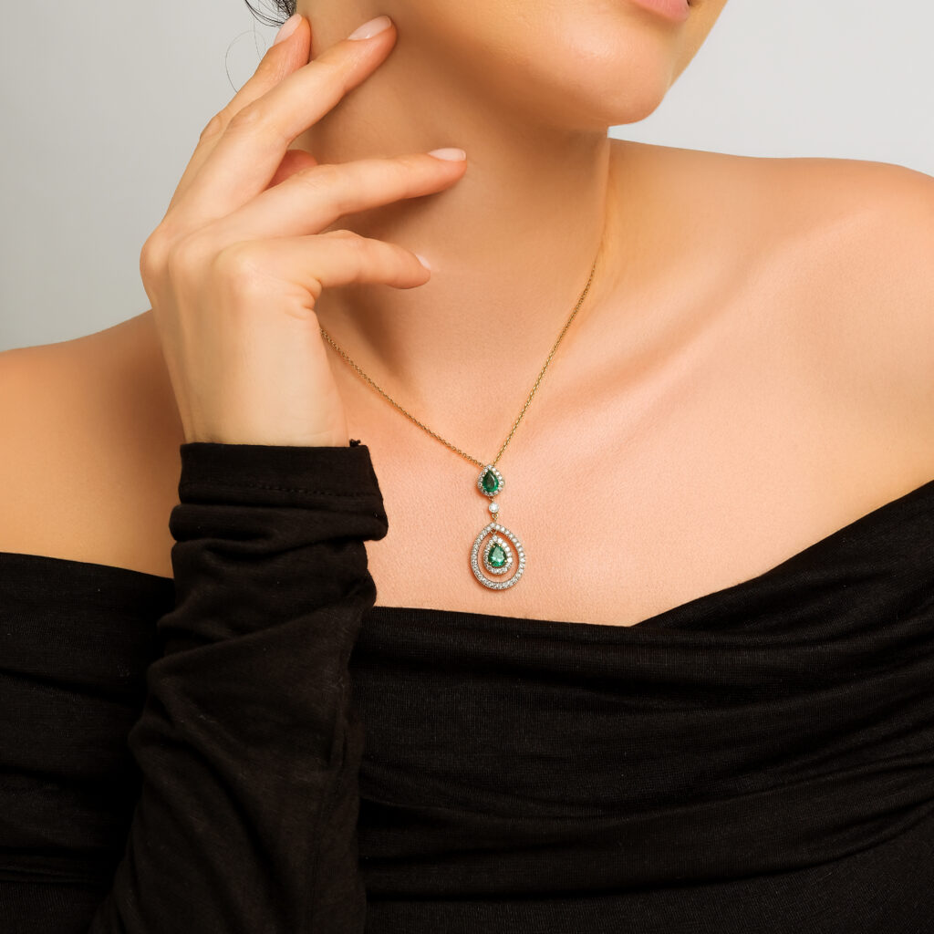 Zümrüt Cascade Necklace — two emeralds framed by diamond halos, yellow gold, worn on neck